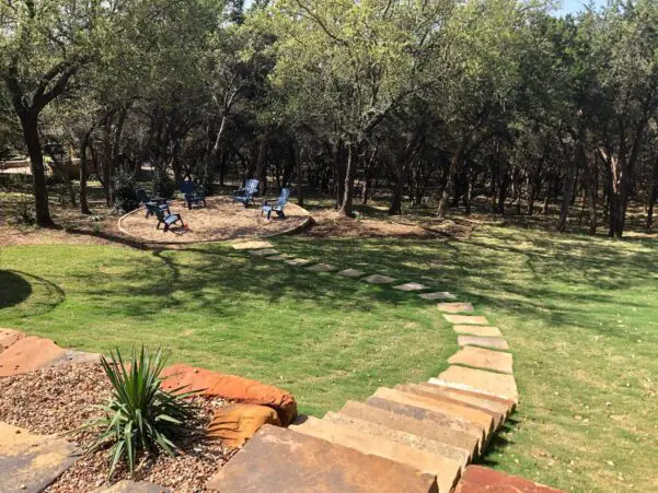 Natural flagstone stairs leading to a circular gravel fire pit area under oak trees in a Dripping Springs backyard