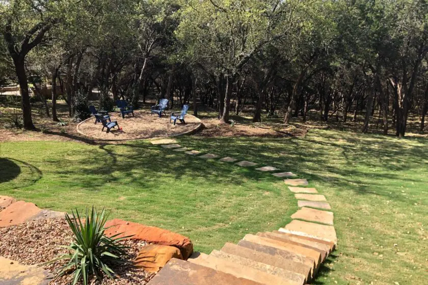 Natural flagstone stairs leading to a circular gravel fire pit area under oak trees in a Dripping Springs backyard