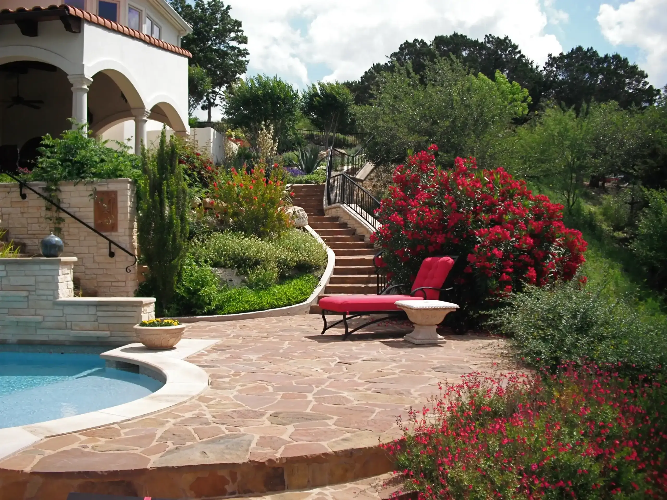 Hillside poolside landscape featuring tiered stone retaining walls, greenery, a flagstone patio, and a scenic valley view.