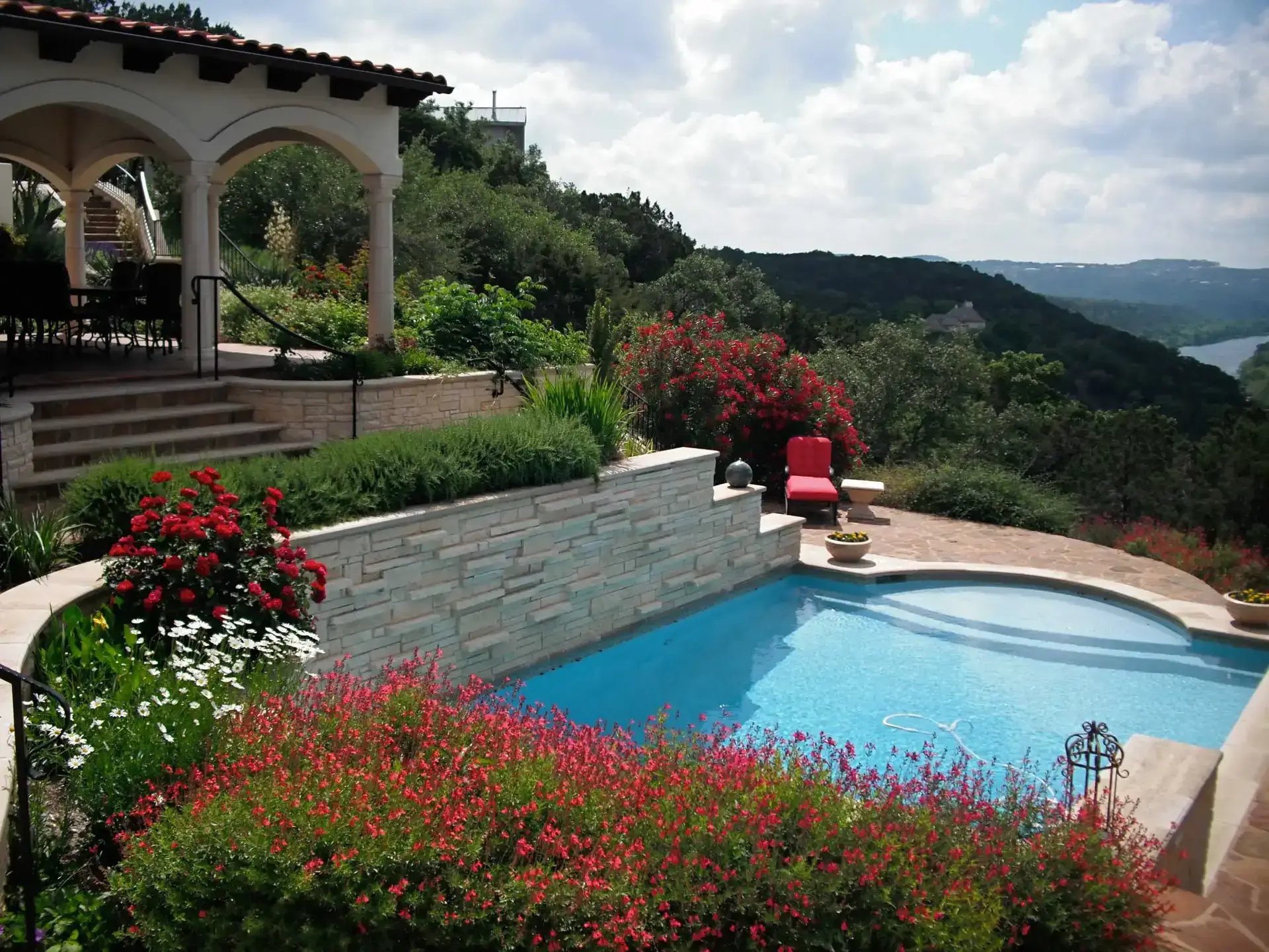 Multi-level luxury landscaping in Westlake Hills, TX featuring a swimming pool, limestone retention walls, vibrant red sage and daisy gardens, and a scenic view of the Texas Hill Country