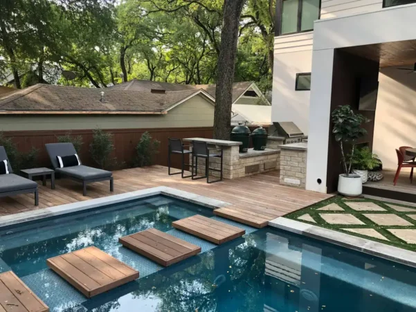 Multi-level luxury landscaping in Westlake Hills, TX featuring a swimming pool, limestone retention walls, vibrant red sage and daisy gardens, and a scenic view of the Texas Hill Country